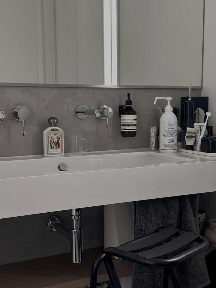 落ち着いたグレーと白の色調のパウダールーム、モダンな洗面台と黒いスツールが配置された清潔感のあるインテリア