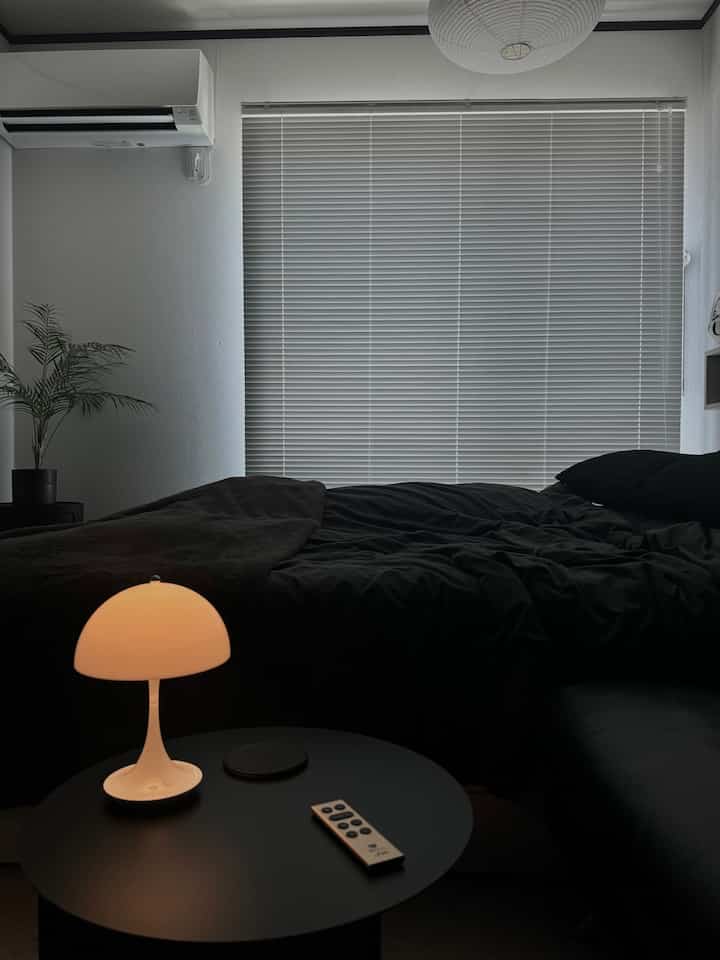 ブラックとホワイトの色調の寝室、丸テーブルの上のテーブルランプとソファが配置されたモダンでミニマルな雰囲気のインテリア