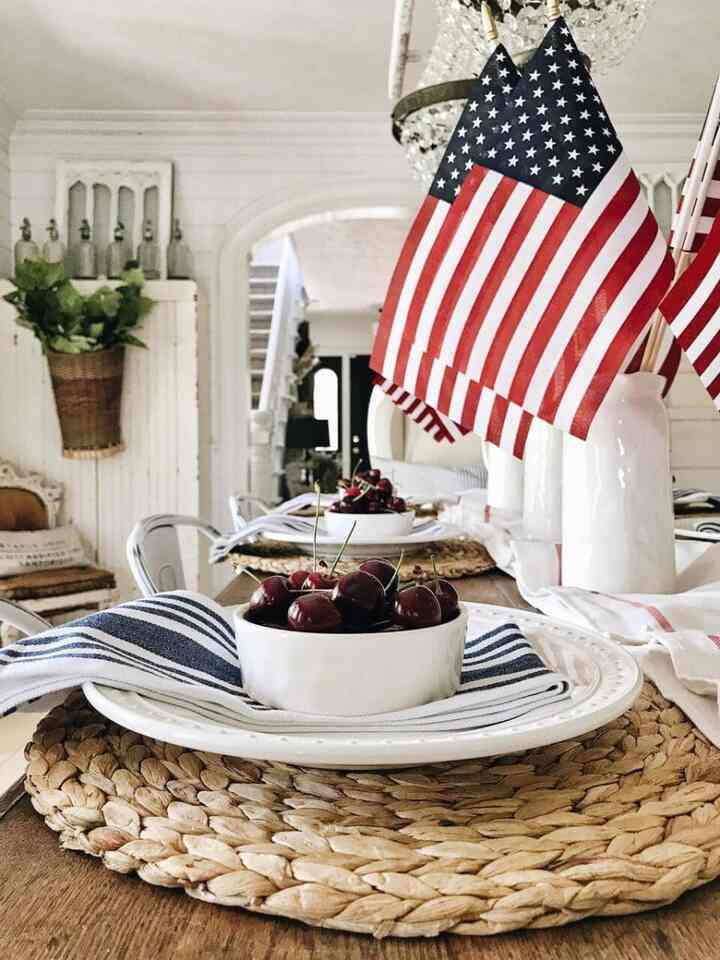 A natural-toned dining room featuring white tableware and round woven placemats with American flag decorations, creating a warm and cozy atmosphere