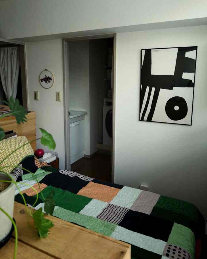 ナチュラルカラーが基調の寝室、パッチワークの掛け布団カバーとモダンなモノクロポスターが配置された落ち着いた雰囲気のインテリア