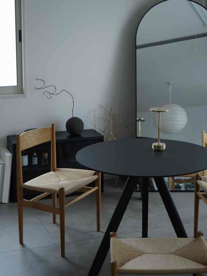 Gray-toned walls and floor with a round black dining table and natural wood chairs in a modern dining room