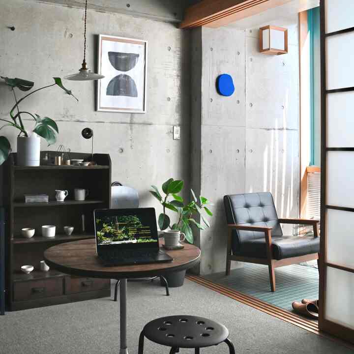 ウッドトーンとブラックを基調としたナチュラルなホームオフィス空間、植物と丸テーブルが配置された居心地の良い小さな部屋