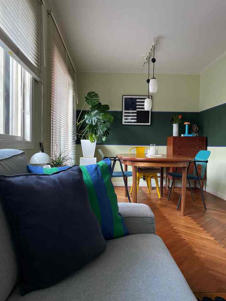 Living room with light and dark green walls, featuring a gray sofa and colorful dining chairs in a warm atmosphere