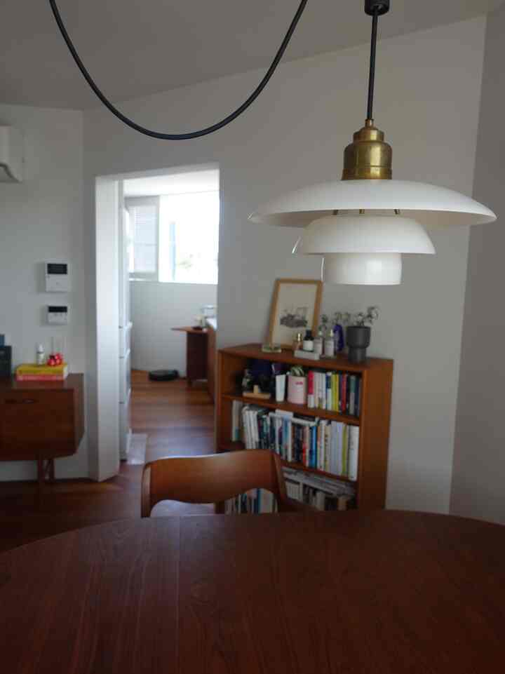 白い壁と木目調家具が調和する北欧風ダイニング、中央にルイスポールセンのペンダントライトが配置された雰囲気のあるインテリア