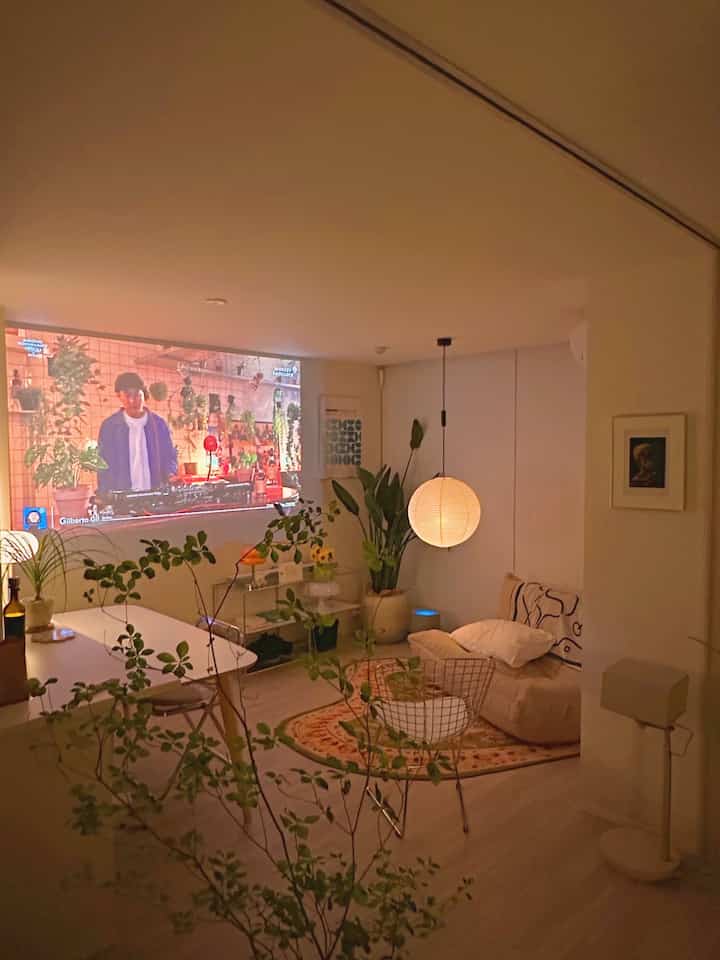 ベージュ調のワンルームリビング兼ホームシネマ、ソファとラグ、大きなペンダントライトが配された雰囲気のある韓国インテリア