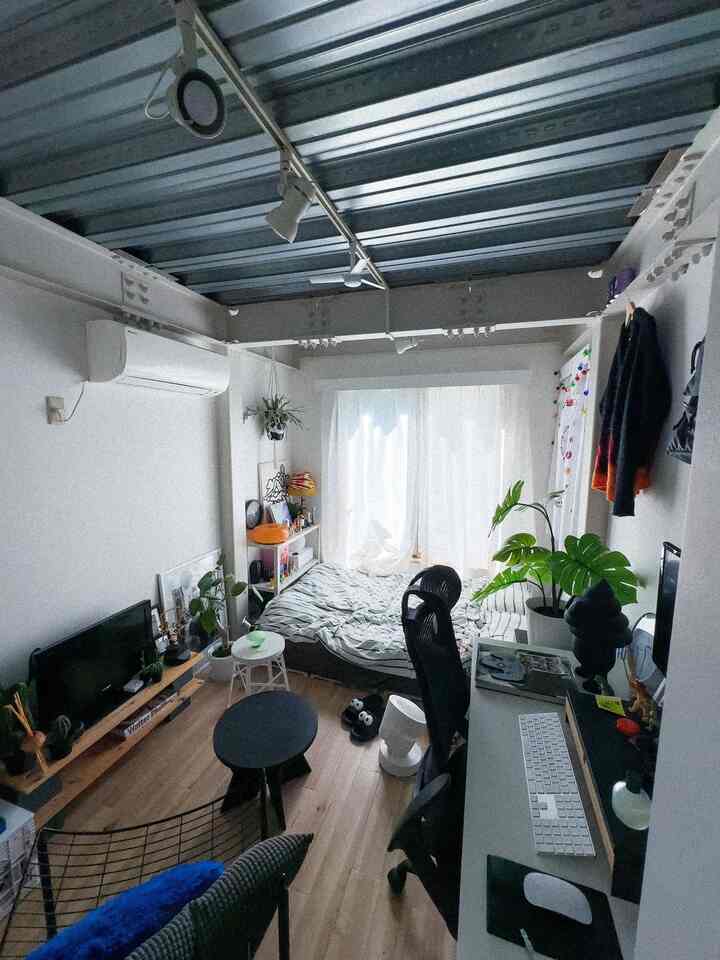 ナチュラルな色調の狭い寝室、デスクとベッド、モンステラの植物が配置された印象的で開放的なインテリア