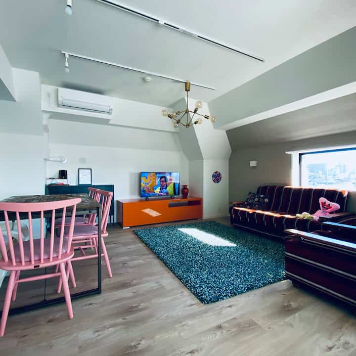 Nordic style living room with wood-toned flooring and pink dining chairs, featuring a clean layout and cozy ambient lighting