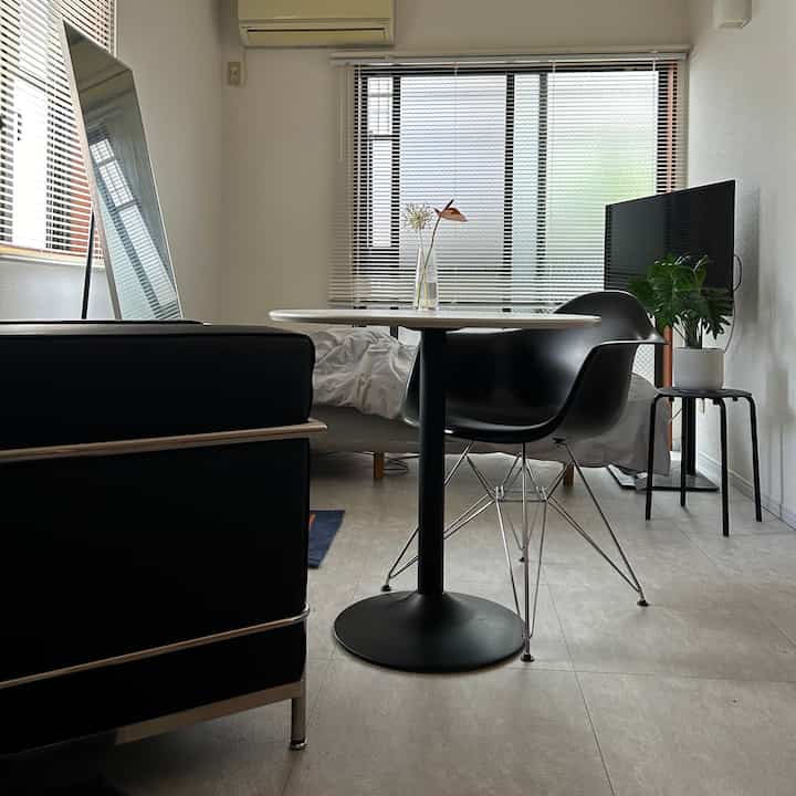 A minimal white-walled living room for a single household featuring black furniture, a round cafe table, and a green plant