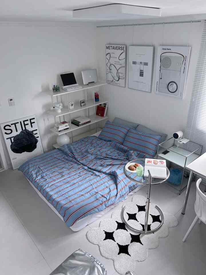 Bright white bedroom with sky blue striped bedding on bed, mid-century modern posters and bookshelf arranged neatly