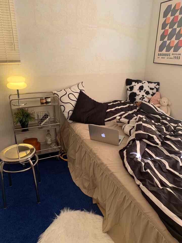 ベージュとネイビーの色調のワンルーム寝室、ステンレス製スツールと無地フリルベッドスカートが配置された印象的な空間