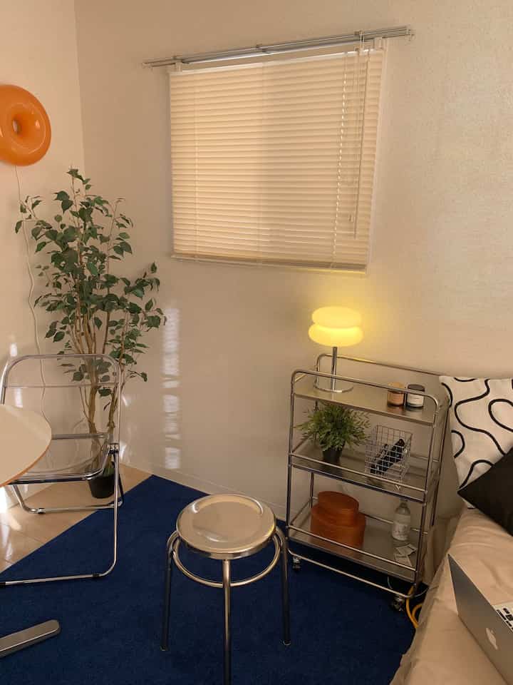 白い壁とネイビーカーペットのワンルーム、ステンレススツールとソファが配置されたナチュラルで落ち着いた雰囲気の空間