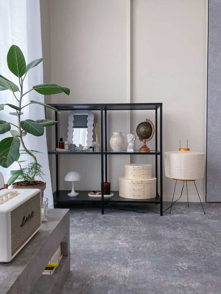 白とグレーの色調のリビング、黒のメタル棚とフロアランプ、植物が配置されたシンプルなインテリア