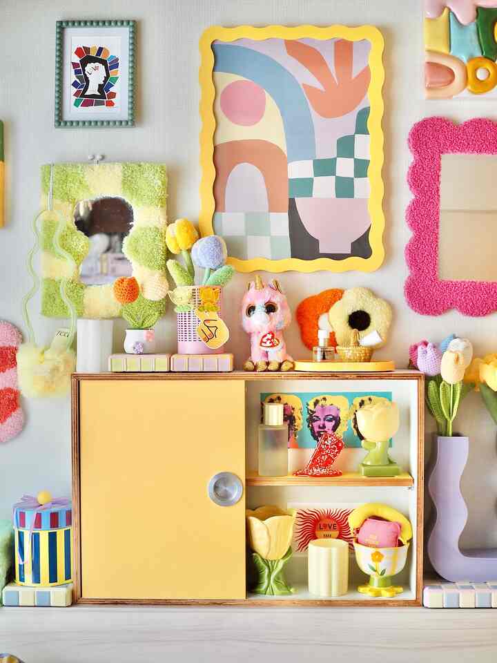 パステルと黄色のトーンが調和する壁装飾と小型キャビネットが配置された北欧風の空間