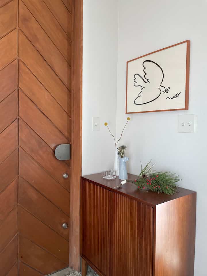 ナチュラルな木目調の玄関、木製の玄関扉とヴィンテージ風のシューズラック、壁に掛けられたアートのある雰囲気のあるインテリア