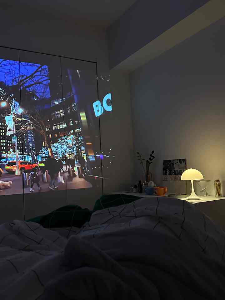 白を基調とした寝室、プロジェクターで壁に映像を映し、テーブルランプの柔らかな光がある雰囲気のあるインテリア