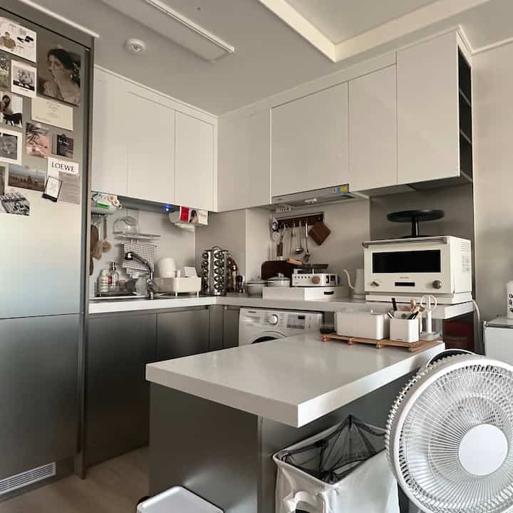 白とグレーのトーンのキッチン、コンパクトな空間に収納アイデアとモダンなキッチンアイランドが配置された清潔感のあるインテリア