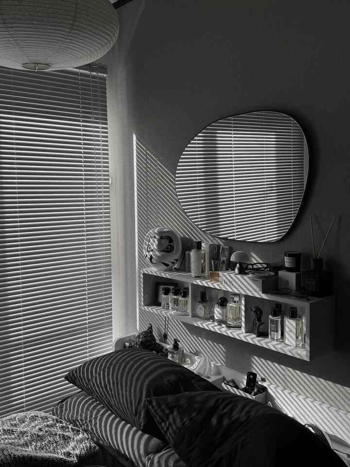 モノトーンのリビング、窓辺のブラインドと不規則な鏡が光の模様を作り、落ち着いた雰囲気の空間