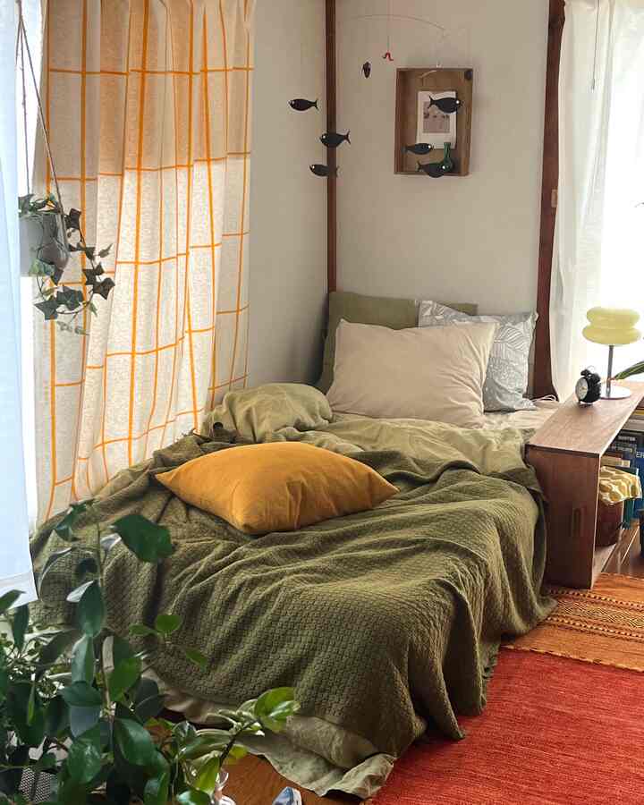 Natural wood tones and green-orange hues in a single household bedroom featuring pillows, curtains, and a fish mobile for a cozy vibe