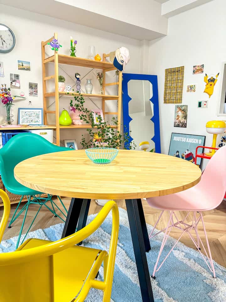 Colorful dining room featuring bright yellow, pink, and green chairs around light wood table, accented by a large blue mirror