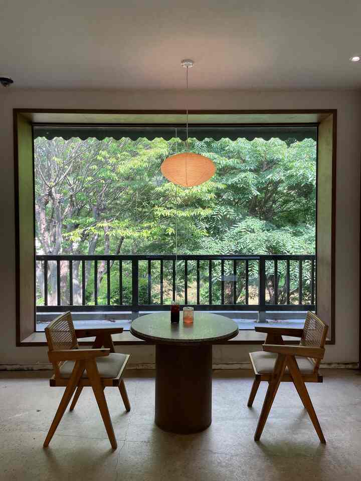 ナチュラルカラーの木目調家具と大きな窓がある二人用のカフェ空間、静かで自然と調和した雰囲気のあるインテリア