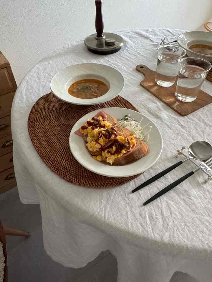 ナチュラルカラーとブラウンのダイニング、白いテーブルクロスと食器、テーブルとカトラリーが配置された雰囲気のあるインテリア