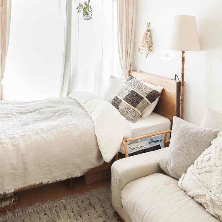 明るくナチュラルな色調のワンルーム寝室、オーク無垢材のベッドとクッション、1人掛けソファを配置した雰囲気のあるインテリア