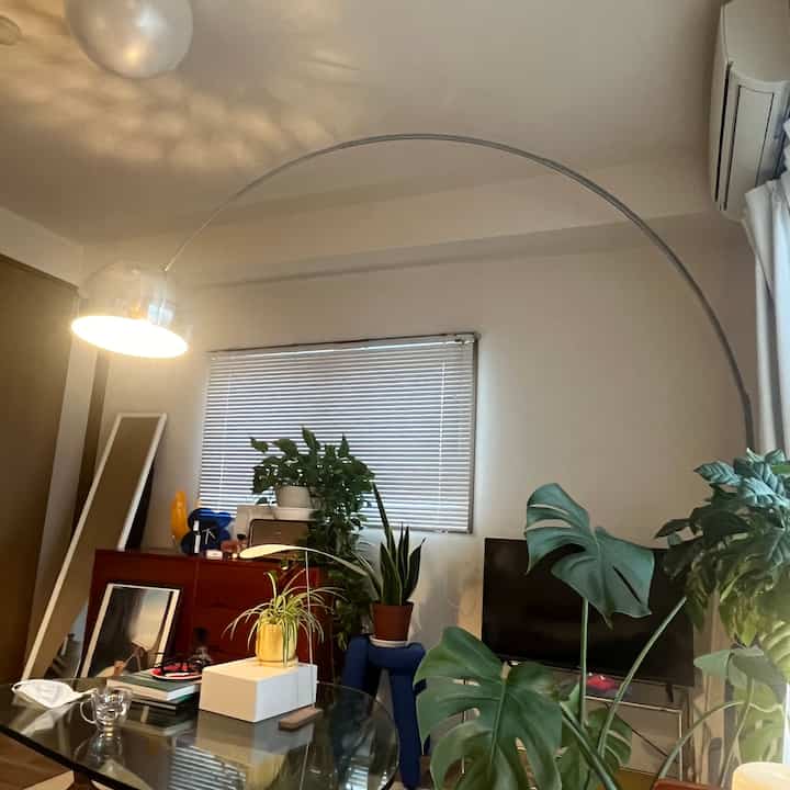 ナチュラルトーンのリビング、観葉植物とブラインド窓、ミッドセンチュリーモダン家具と間接照明が配置された落ち着いた空間