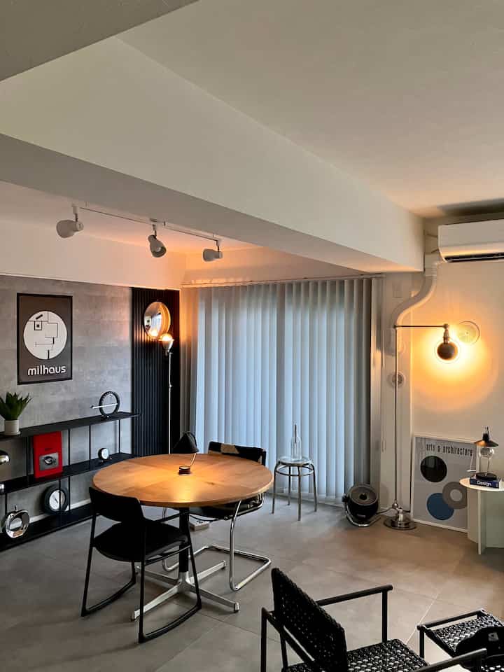 暖かい間接照明が映えるモノトーンのインダストリアルスタイルのキッチンスペース、丸いダイニングテーブルとフロアランプが配置された落ち着いた雰囲気のインテリア