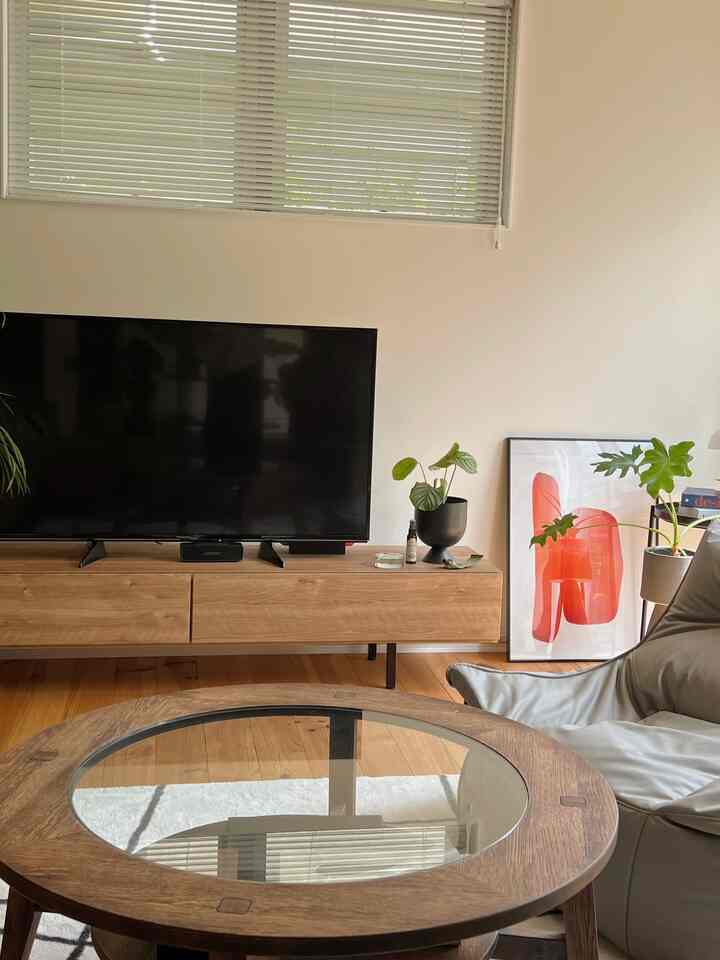 木目調と白を基調とした北欧風リビング、テレビ台と丸いローテーブル、ポスターと植物が配置された温かみのあるインテリア