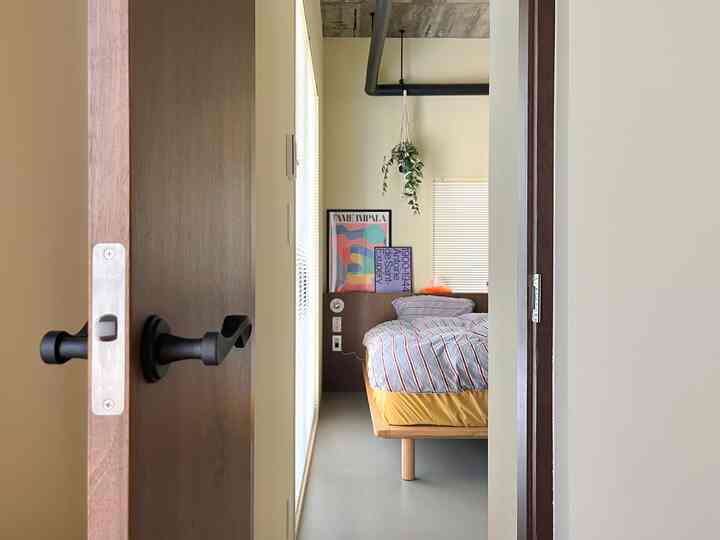 ベージュと木目調の寝室、ストライプの寝具とポスター、植物が配置されたシンプルで自然な雰囲気のインテリア