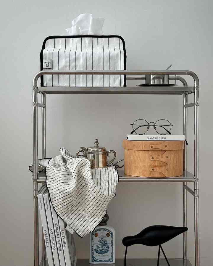 白い壁を背景にしたステンレス製の移動式トロリーに多様な小物と収納アイテムが置かれたシンプルなおうちカフェ空間