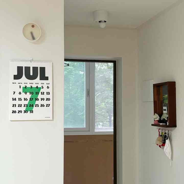 明るいホワイトトーンの玄関、木製の鏡と壁掛けカレンダーが配置されたすっきりとした空間