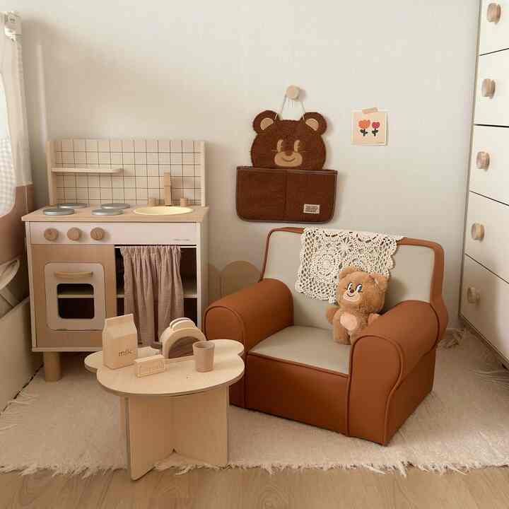 Natural-toned kids' room featuring a brown baby sofa and wooden play kitchen set in a cozy atmosphere