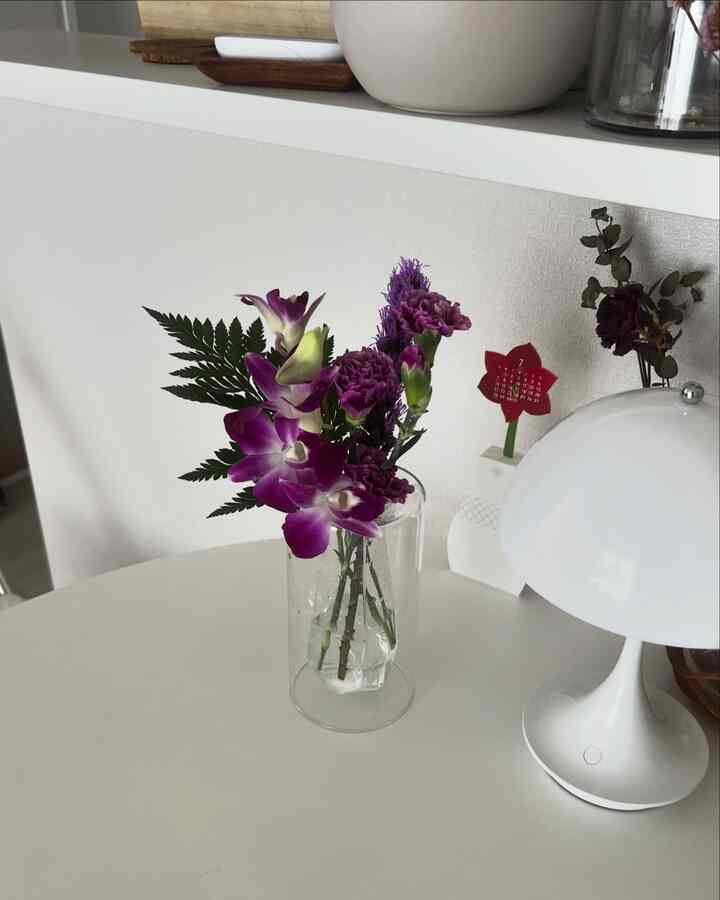 白いテーブルに透明な花瓶と紫の花が置かれたナチュラルでシンプルな雰囲気のインテリア