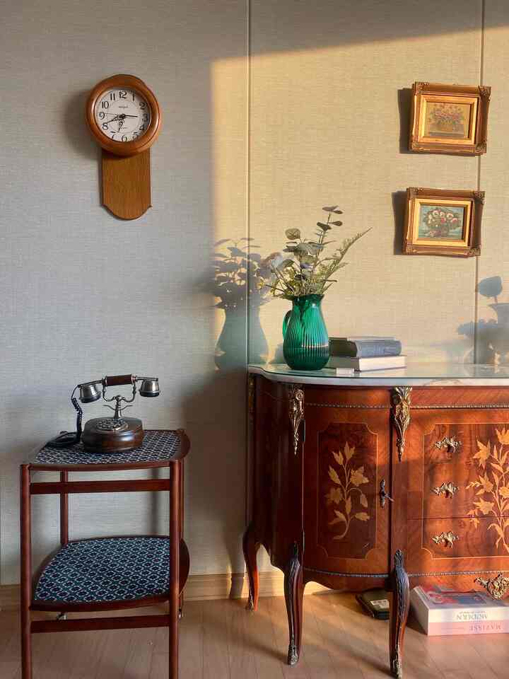 Warm brown wood-tone living room featuring an antique ornate dresser, small trolley, and a green vase with flowers, creating a classic ambiance