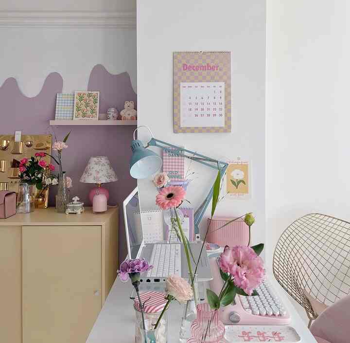 White background home office with pink and purple accents, featuring a desk with flowers and a gold wire chair, creating a cozy workspace