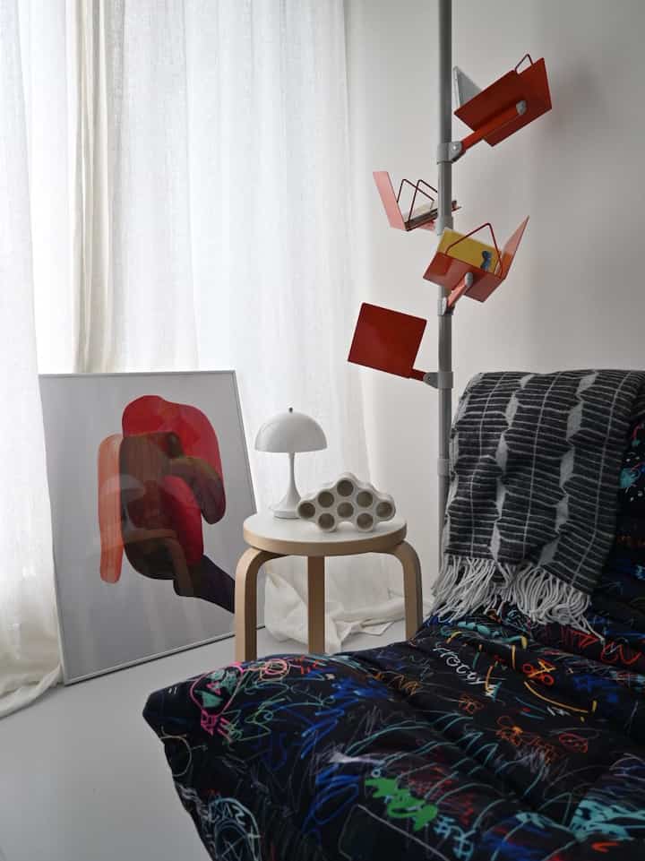 白いカーテンと薄い木製のスツール、赤いポスター、多機能な赤いファイルホルダーが置かれたモダンで芸術的なリビング空間