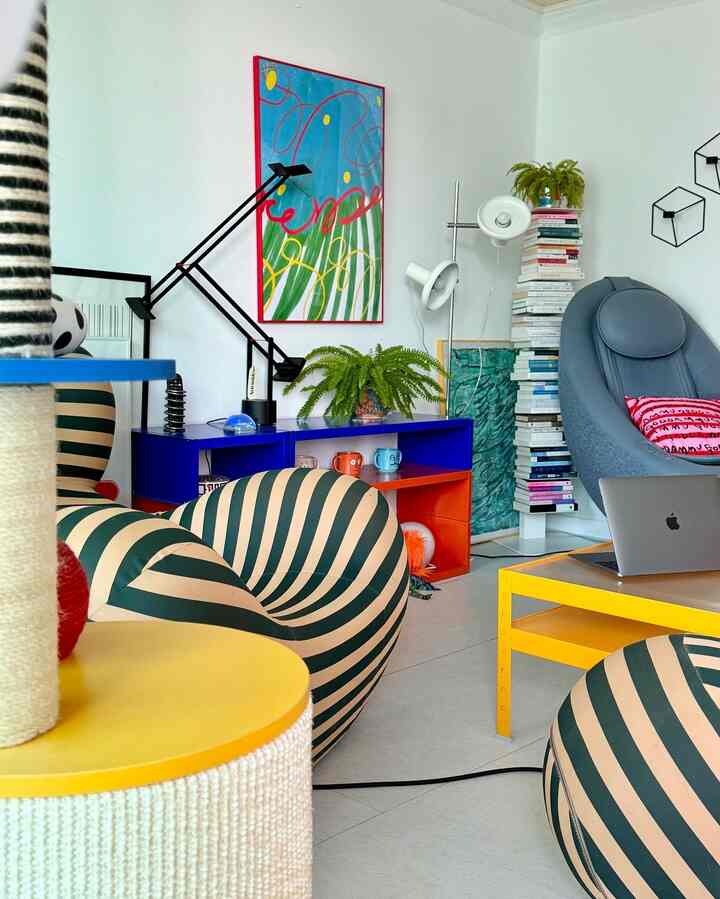 明るいイエローとブルーのトーンが際立つコンパクトなリビングルーム、ストライプのビーズクッションとモダンな家具が配置され、快適で活気あふれる雰囲気を演出しています。