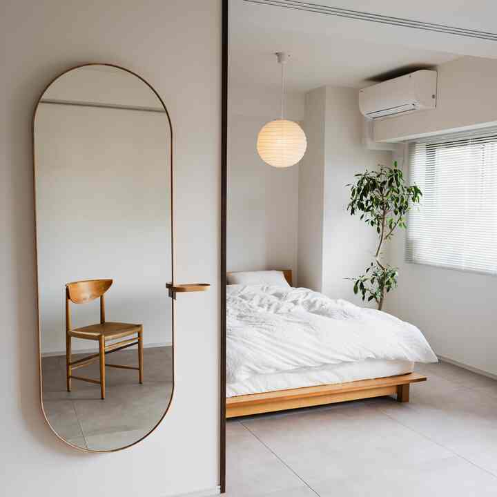 White and wood-tone bedroom with large floor mirror and simple pendant lighting, creating a clean and natural atmosphere