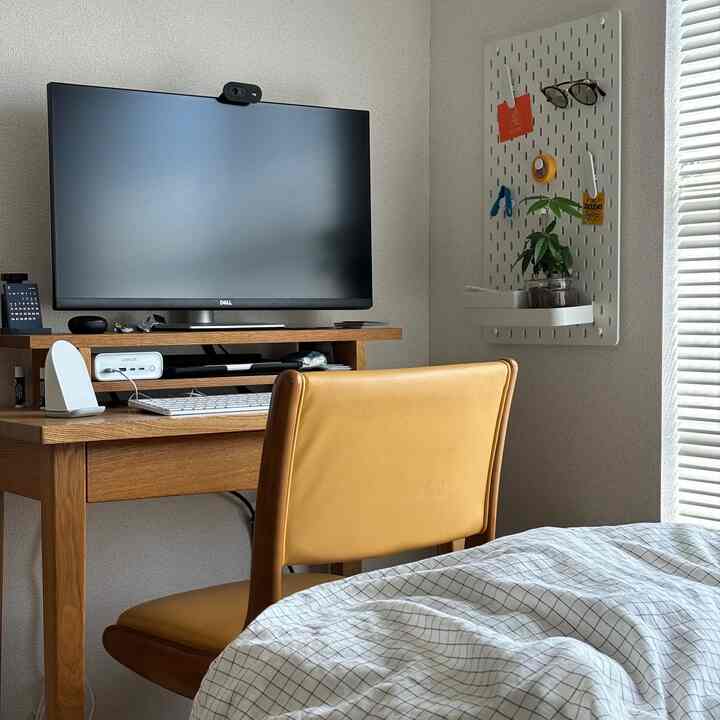 白い壁と茶色の木製デスクが配置されたナチュラルな雰囲気の一人暮らし用狭小ホームオフィス兼寝室のインテリア