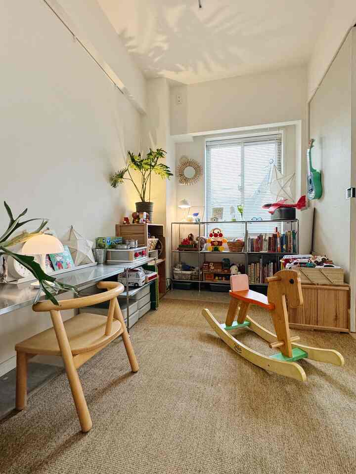 白い壁とナチュラルな木製家具が調和した小さな子供部屋、おもちゃ棚と木製のロッキンホースが配置された温かみのあるインテリア