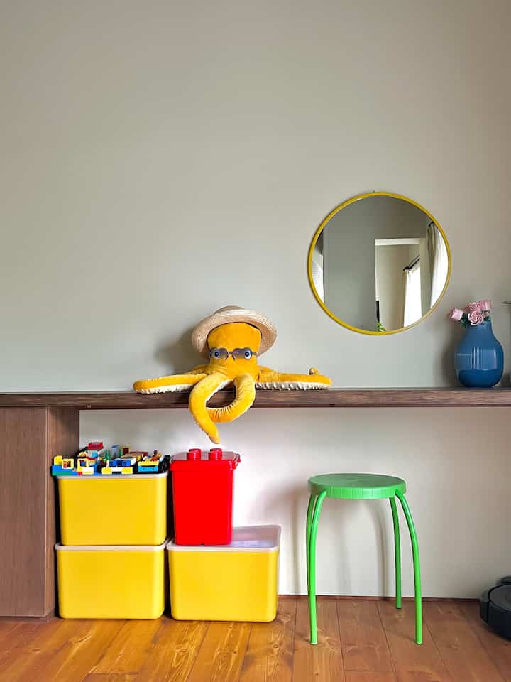 Yellow and green toned living room featuring counter table with yellow plush octopus and colorful toy storage boxes, creating a neat space