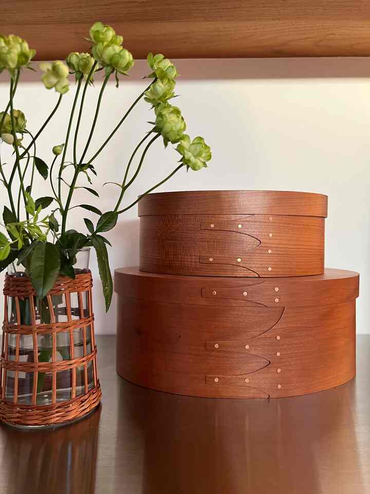 ナチュラルな木目調の丸い収納箱とラタン装飾の花瓶が置かれたシンプルな空間。