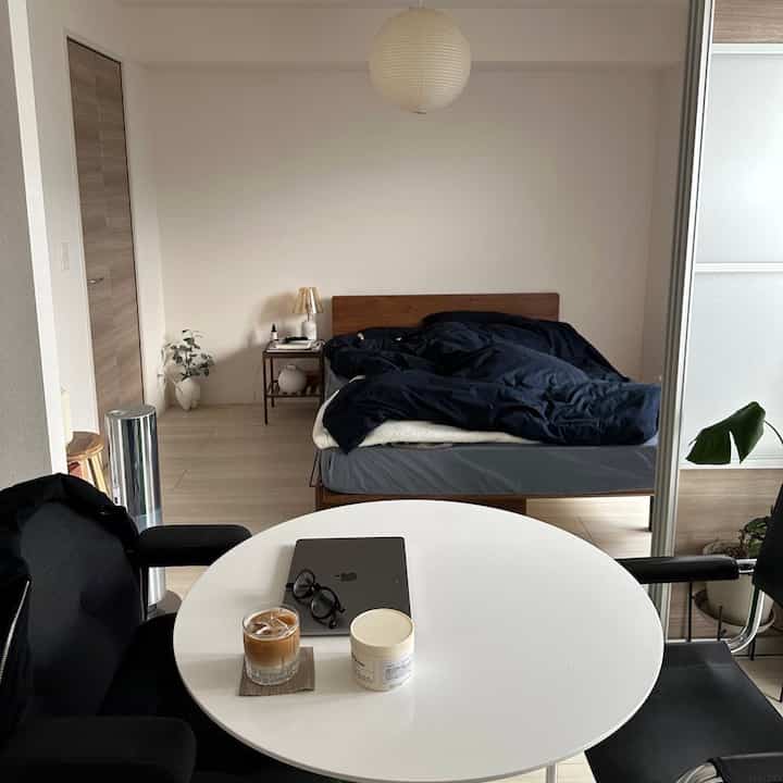 White-walled natural wood bed single-person modern bedroom, featuring a round table and office chairs in a cozy setting