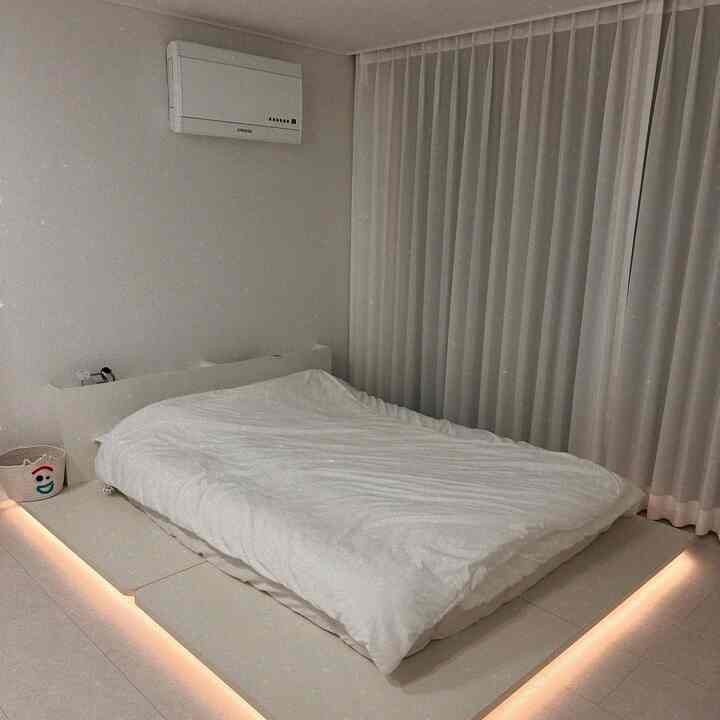 White-toned bedroom featuring a low bed with headboard and ambient indirect lighting, simple and clean space