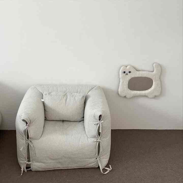 ベージュとブラウンのトーンの子供部屋、ストライプ柄のソファと可愛らしい猫型の鏡が配置された清潔感のある空間