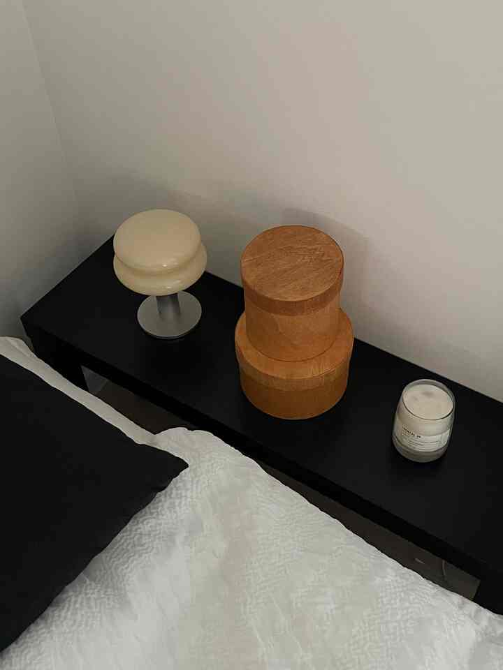 黒いナイトテーブルの上に丸い木製ボックスとキャンドルが置かれた寝室の一角