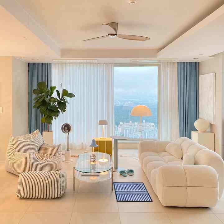 White and blue toned living room featuring curved sofa, bean bag seating, curtains, and floor lamp in a simple modern interior