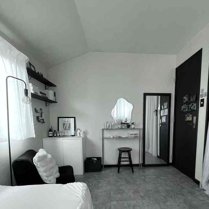 A compact monochrome bedroom with white and black tones, featuring simple furniture and an organic-shaped mirror creating a clean space