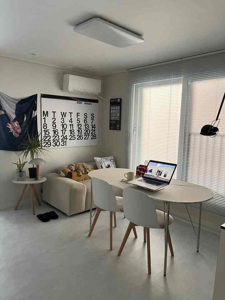 White and gray toned living room and home office featuring sofa, table, calendar, and blinds in a simple modern setup